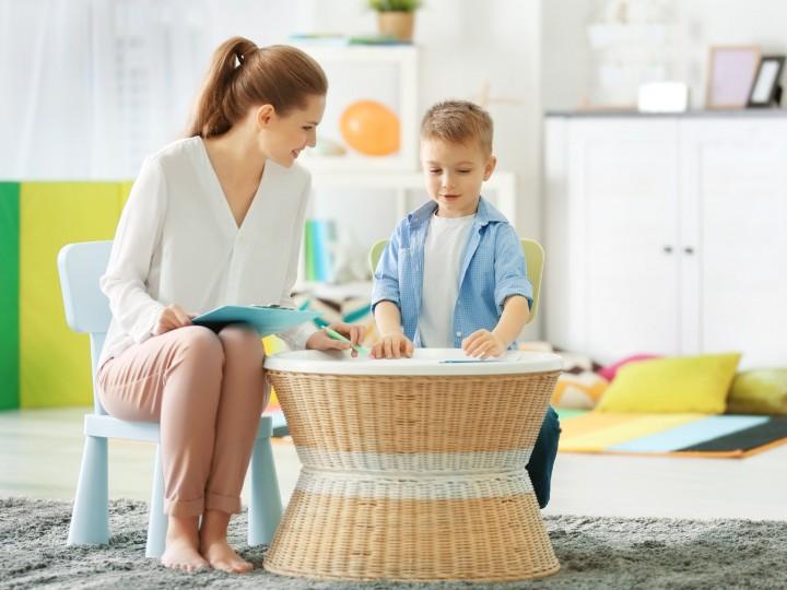 A psychologist holds a notebook and sits at a table with a child